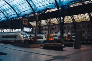 The interior of the Estació de França. On the tracks, there are various trains stationed: a medium distance 449 train, two Rodalies 447 trains, as well as one double-decker Rodalies 450 train. The roof on top is covered with a blue net.