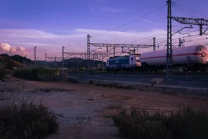 A Renfe cargo train goes by an empty field under the purple sky.