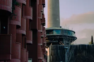 The bottom of a tall concrete tower, which looks like a spacecraft, is visible behind the red façade of the Walden 7 building. It has many small rounded tiled balconies that protrude from the building. 