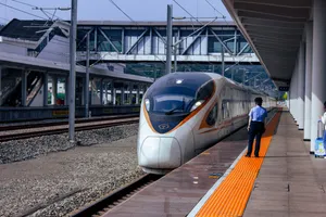 A CR400B high speed train pulling into the station. There's a railway worker standing on the platform watching the train.
