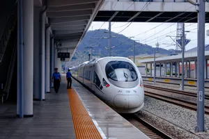 A CRH380C high speed train pulling out of a station, as a railway worker on the platform watches it.