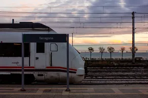 A Renfe 449 train at Tarragona train station, behind the station name sign. The sea is visible on the background.
